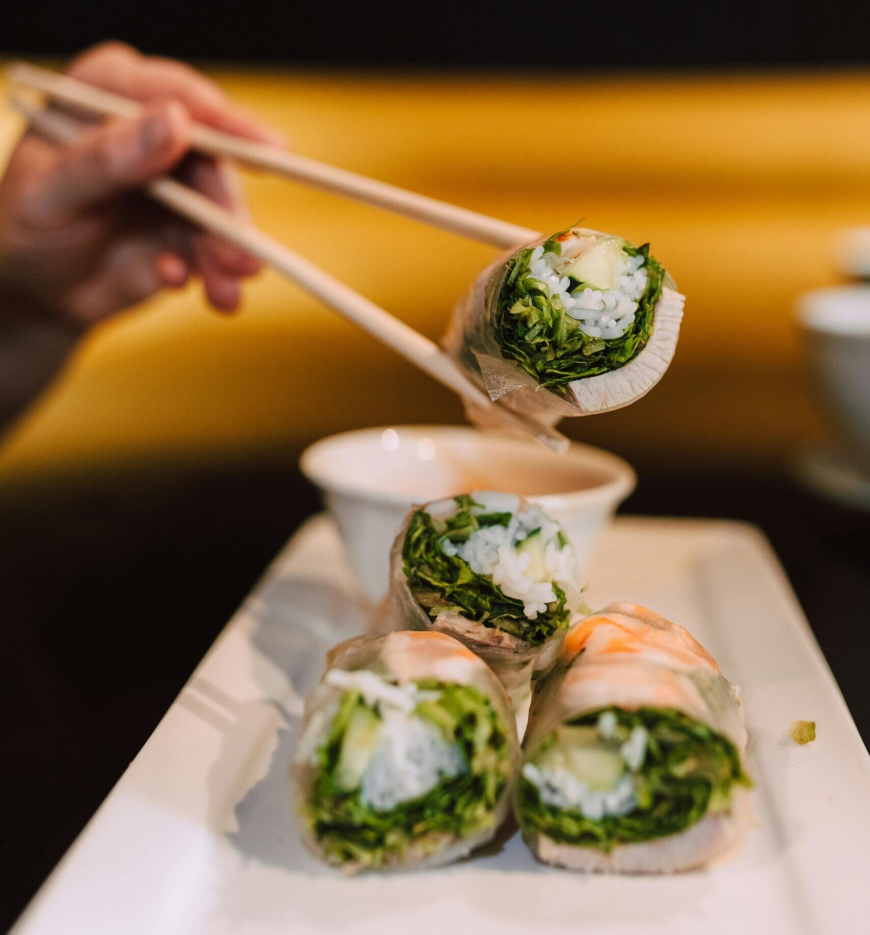 Delicious spring rolls being picked up by chopsticks, showcasing vibrant Asian cuisine.